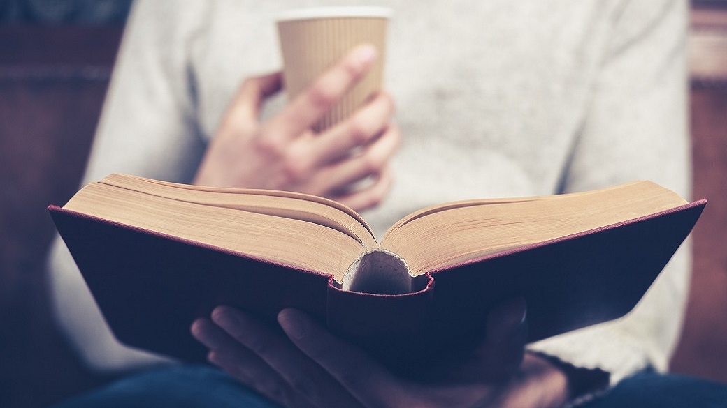 view of an open book and a coffee cup held by a person